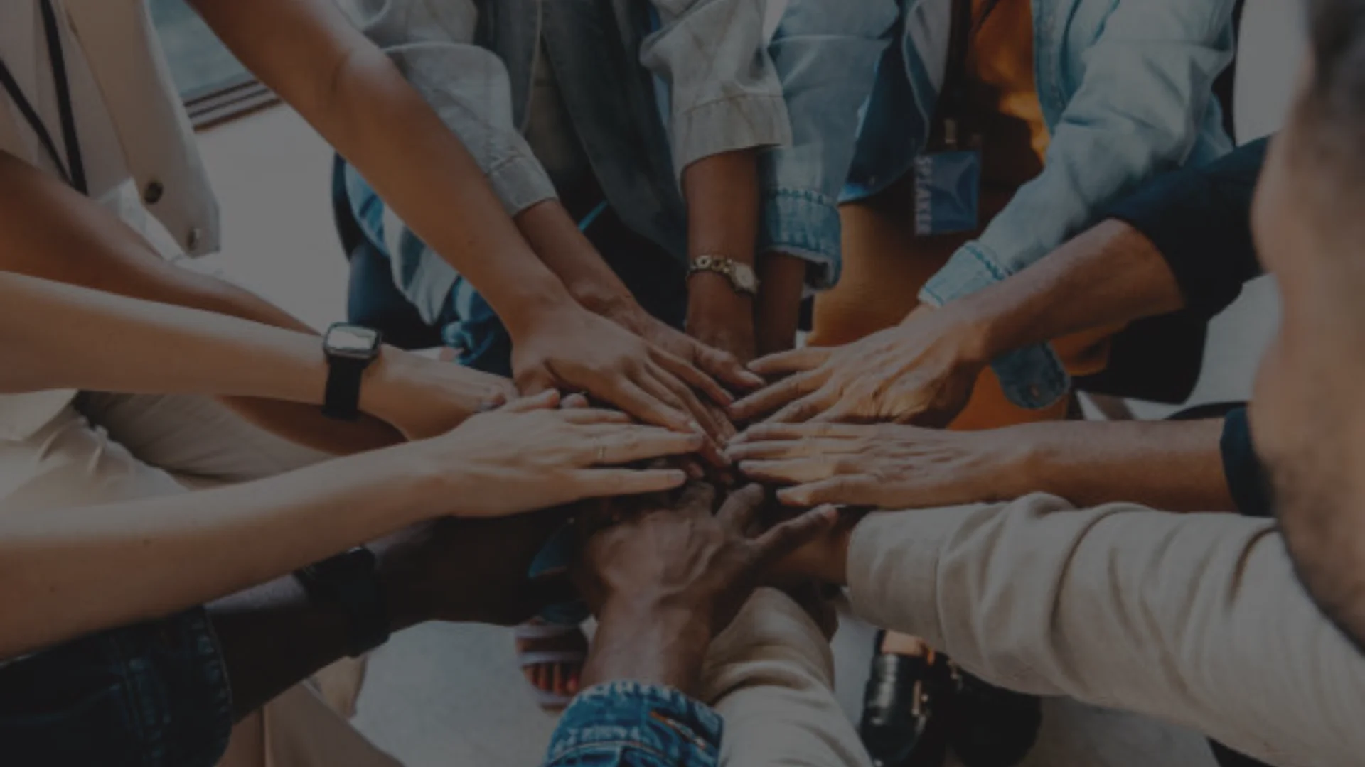 Group of diverse hands stacked together in a circle, symbolizing teamwork.
